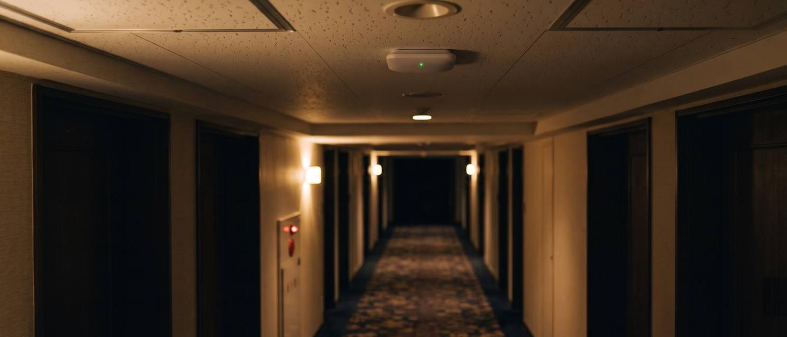 夜のホテル廊下の天井に設置された無線アクセスポイント。ステータスランプが緑に点灯している